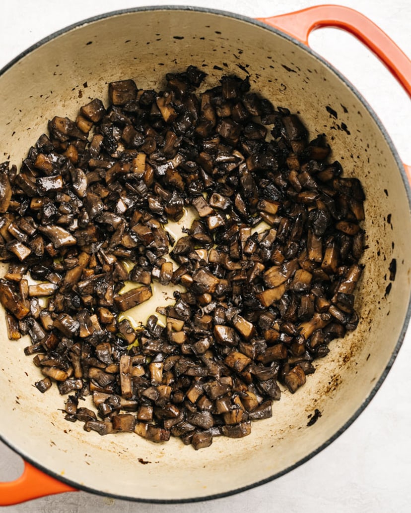 Portobello mushrooms sautéed until crisp and water content is released in a red dutch oven.