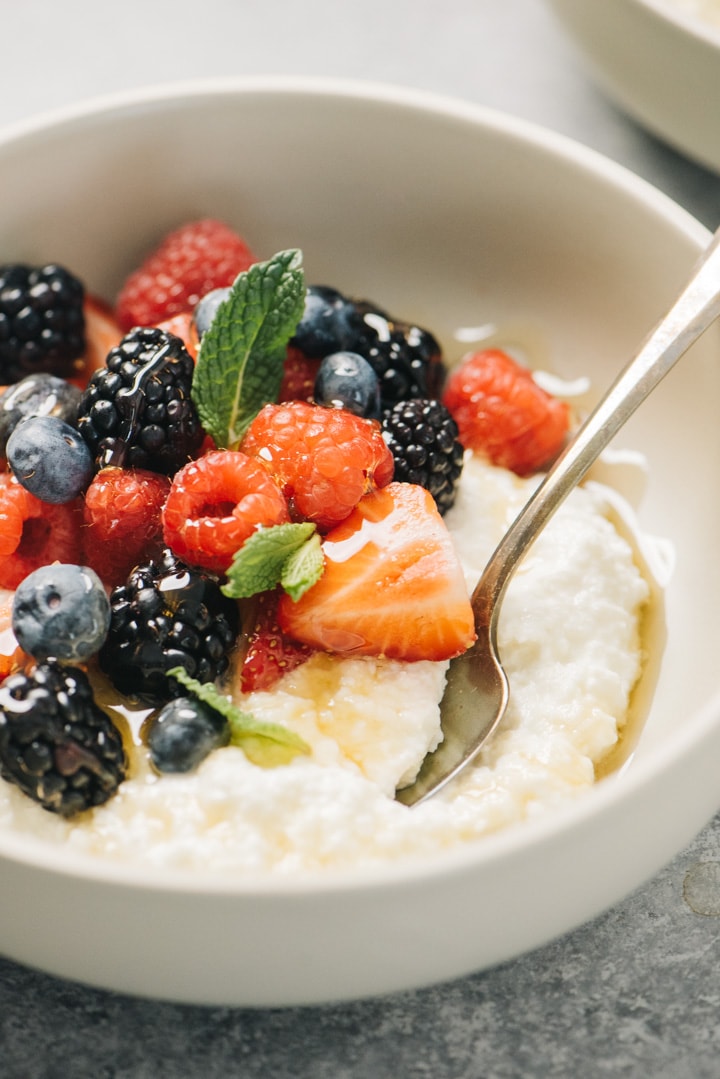 Side view, a spoon tucked into a bowl of homemade ricotta cheese topped with berries and honey.