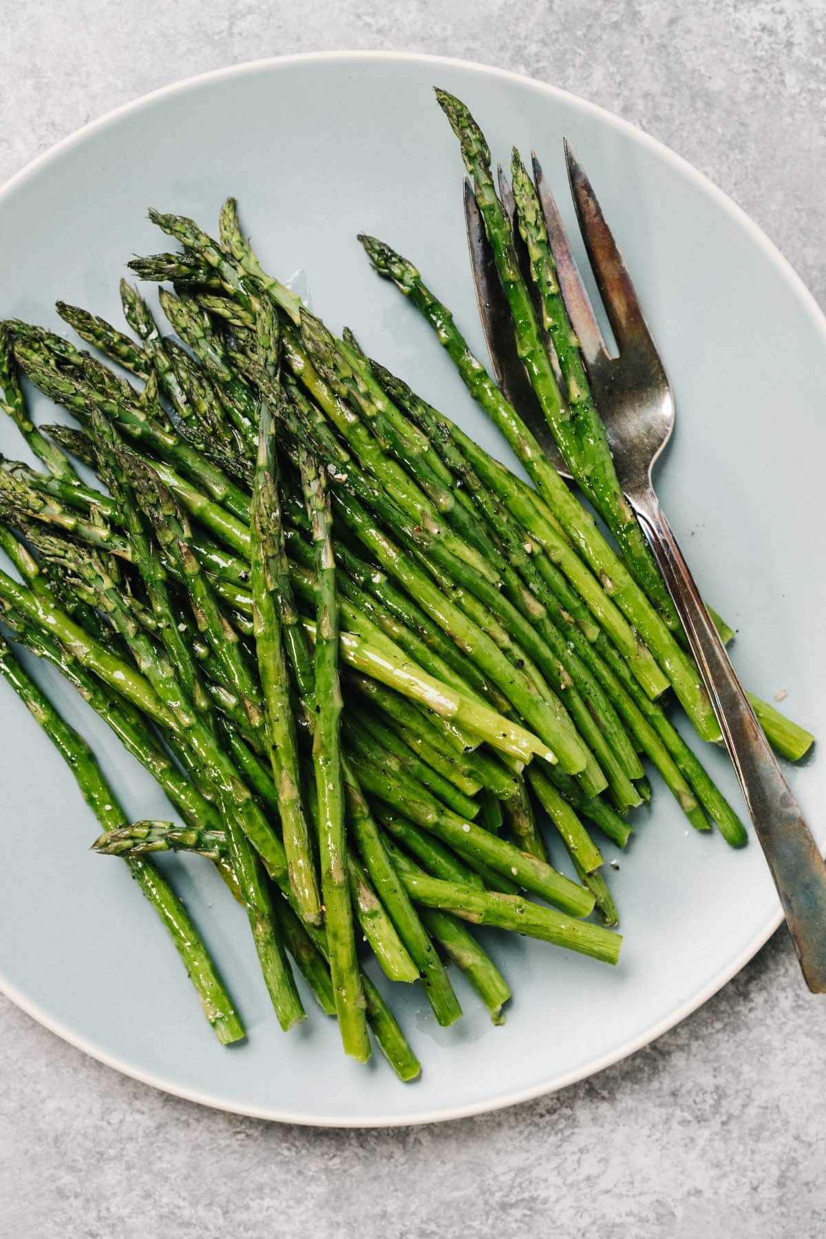 Roasted asparagus on a blue plate with a serving fork.