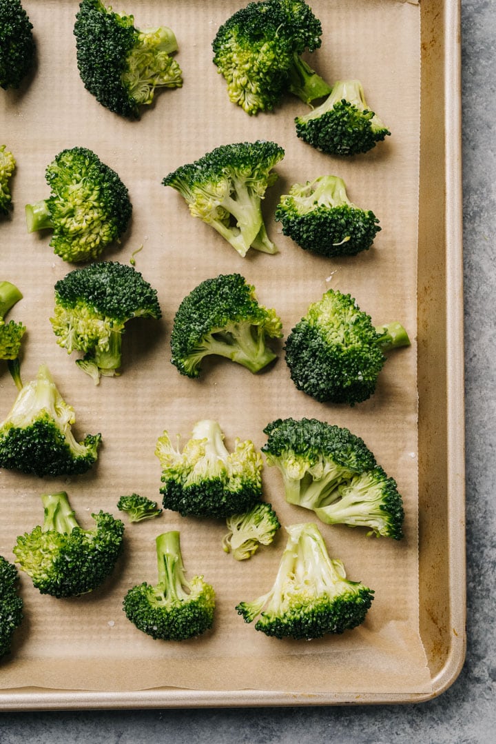 Broccoli florets tossed with olive oil in salt arranged in a single layer on a parchment lined baking sheet.