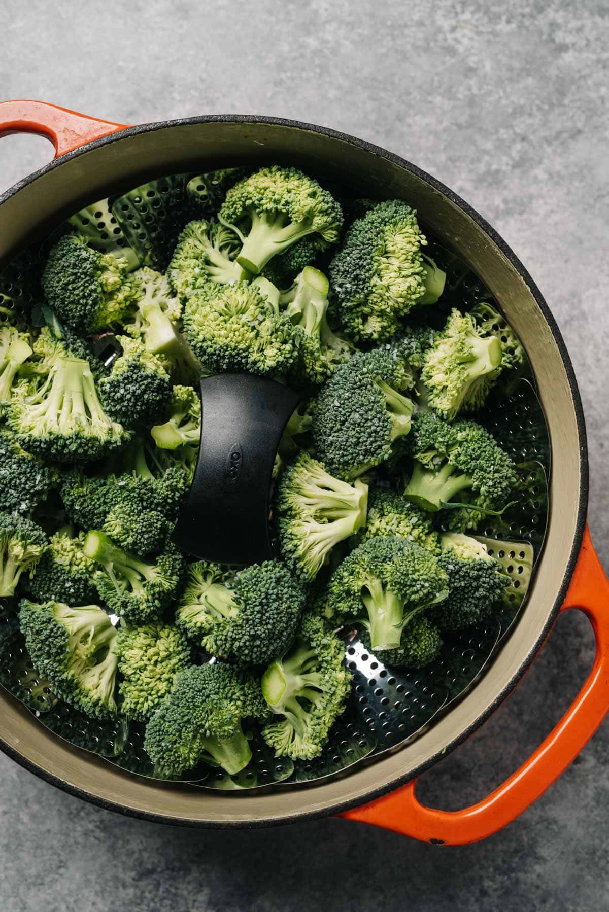Raw broccoli florets in a steamed basket fitted into a dutch oven pot.