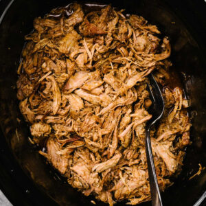 A serving fork tucked into a crockpot filled with slow cooker pulled pork.
