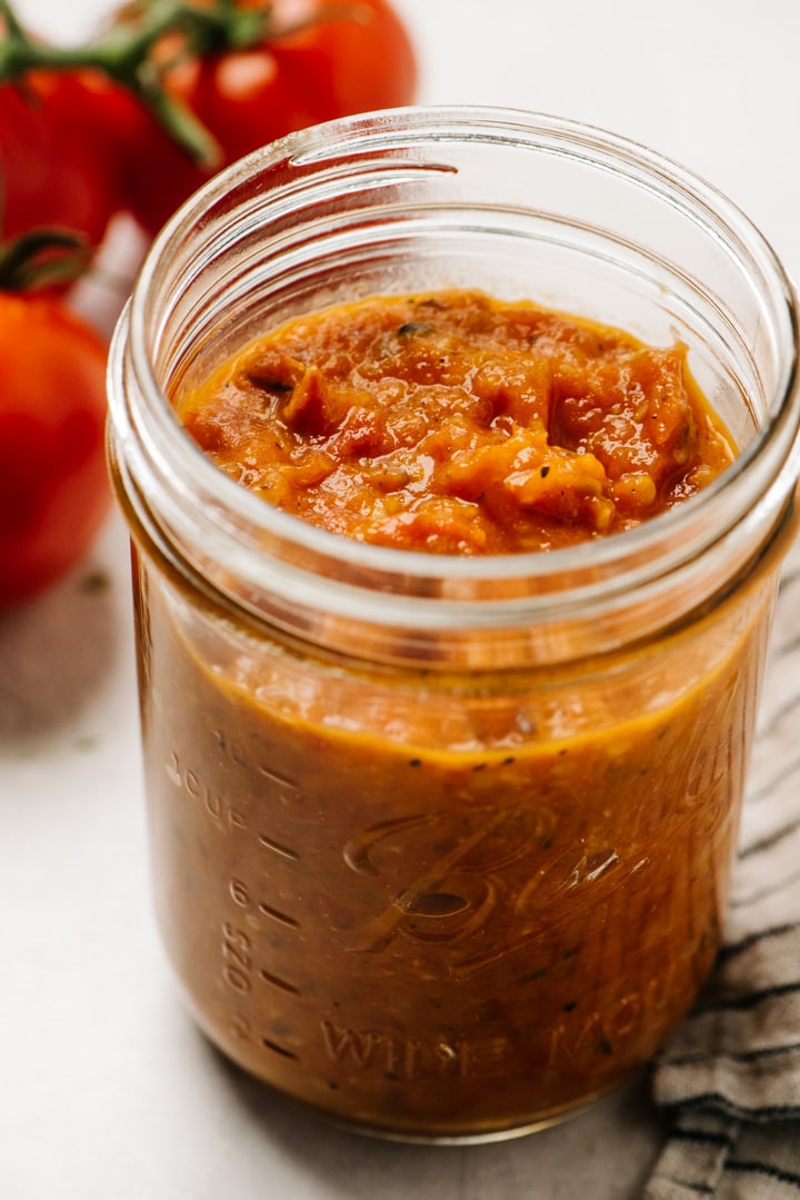 A mason jar filled with marinara sauce with fresh tomatoes in the background.