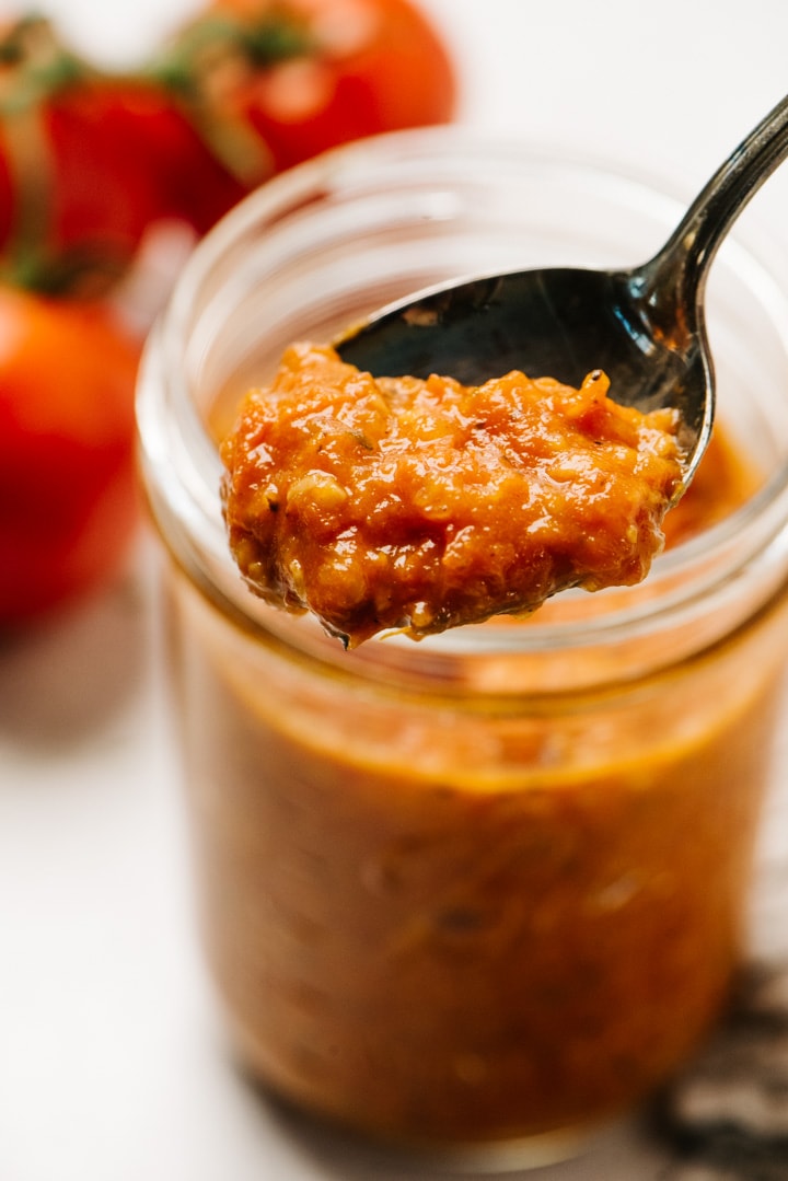 A spoonful of homemade tomato sauce with fresh tomatoes hovering over a mason jar.