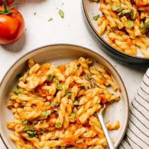 Two bowls of short pasta tossed with fresh tomato pasta sauce with ripe tomatoes and a striped linen napkin to the side.
