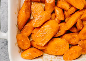 Sliced carrots tossed with spiced honey butter in a casserole dish.