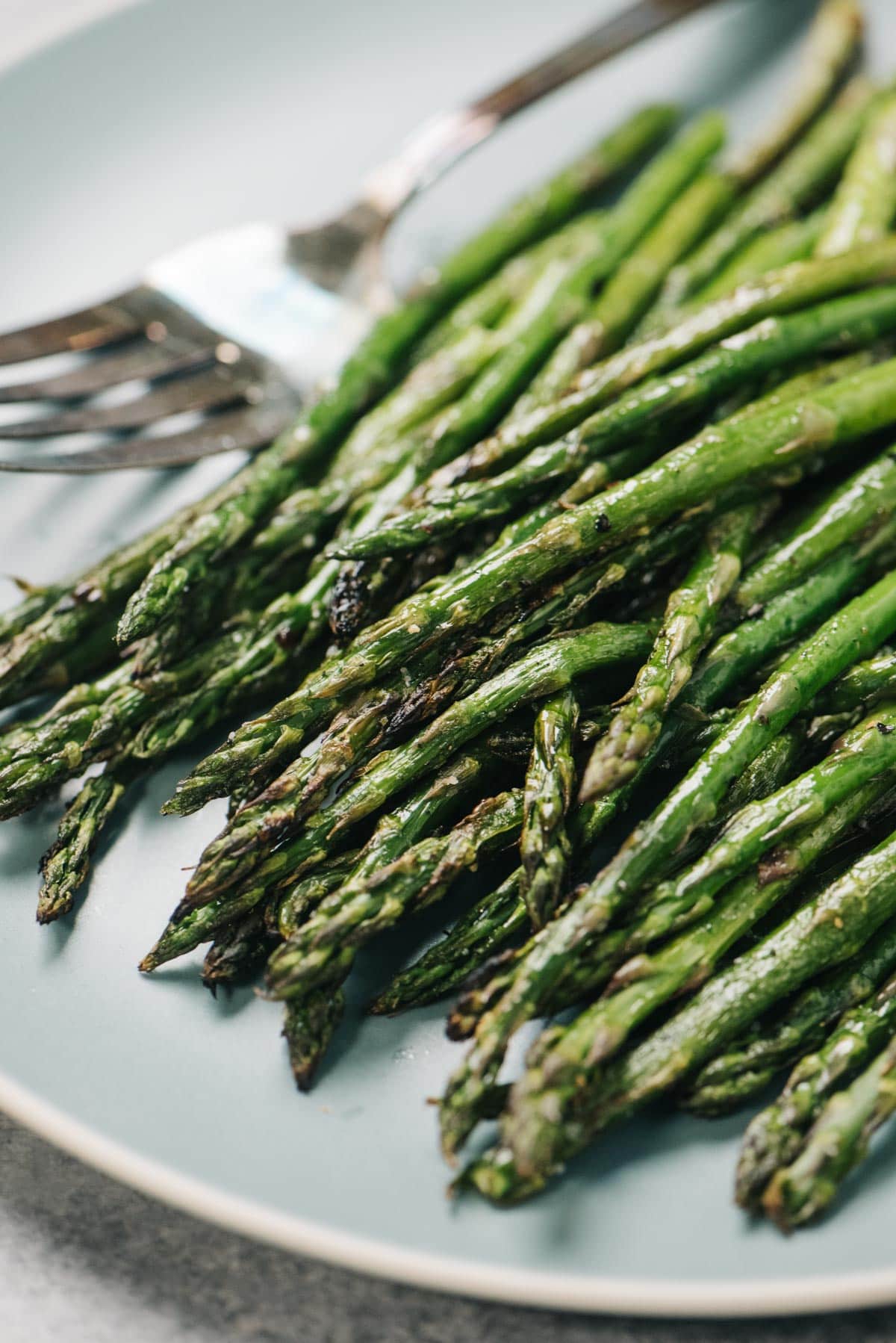 Side view, grilled asparagus on a blue plate with a silver serving fork.