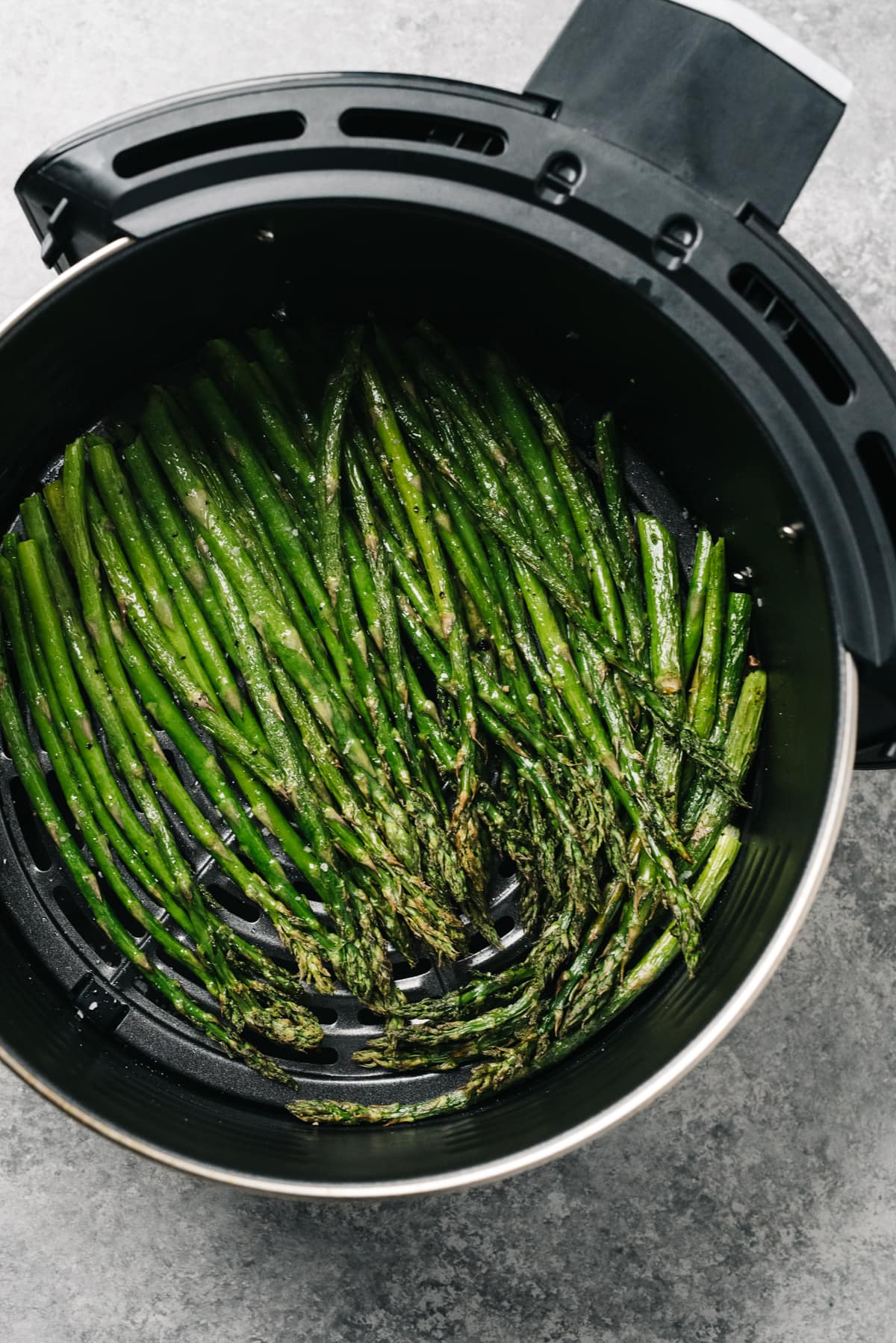 Cooked asparagus spears in the basket of an air fryer.