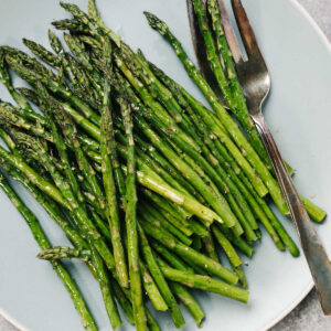 Cooked asparagus on a blue platter with a silver serving fork.