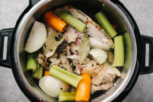 Chicken bones and vegetables covered with filtered water and topped with salt, peppercorns, and bay leaves in an instant pot.