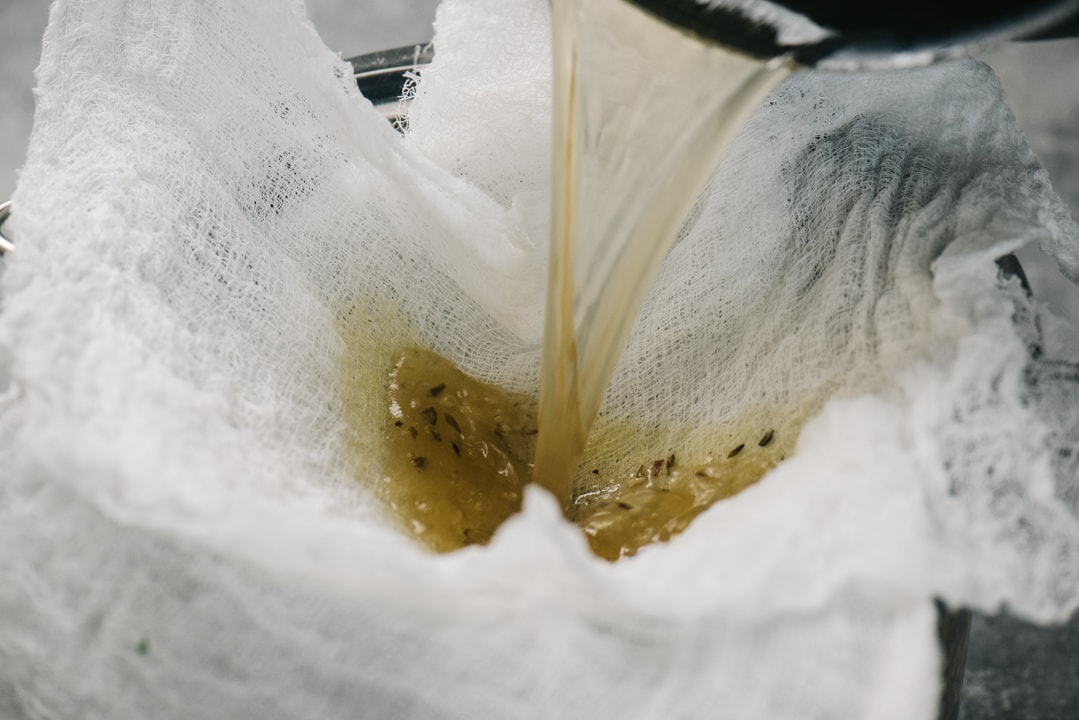 Filtering chicken bone broth through cheesecloth.