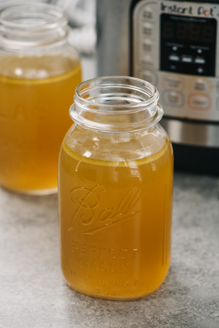 Several mason jars of chicken bone broth in front of an instant pot.