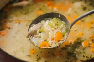 A ladle of chicken orzo soup showing the orzo cooked through in broth.