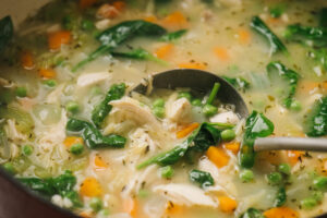 Side view of lemon chicken orzo soup with peas and spinach in a red dutch oven.