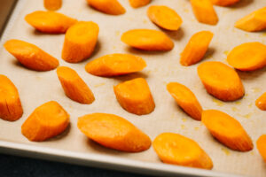 Sliced carrots tossed with olive oil, salt, and pepper on a parchment lined baking sheet.