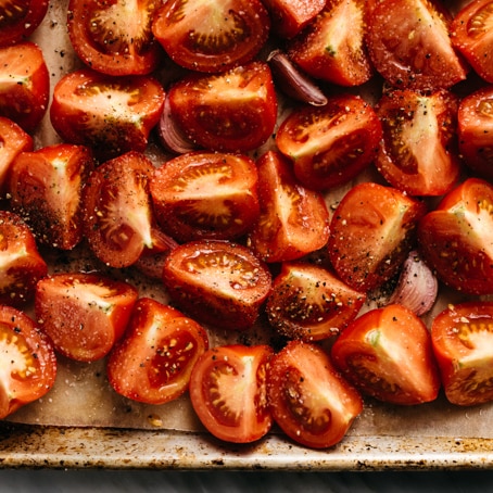 Fresh tomatoes and garlic cloves tossed with olive oil, salt, and pepper on a parchment lined baking sheet. 