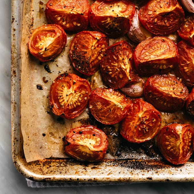 Roasted tomatoes and whole roasted garlic cloves on a parchment lined baking sheet.