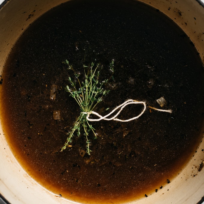 A bundle of fresh thyme in a dutch oven with broth, balsamic vinegar, onions, and dried herbs.