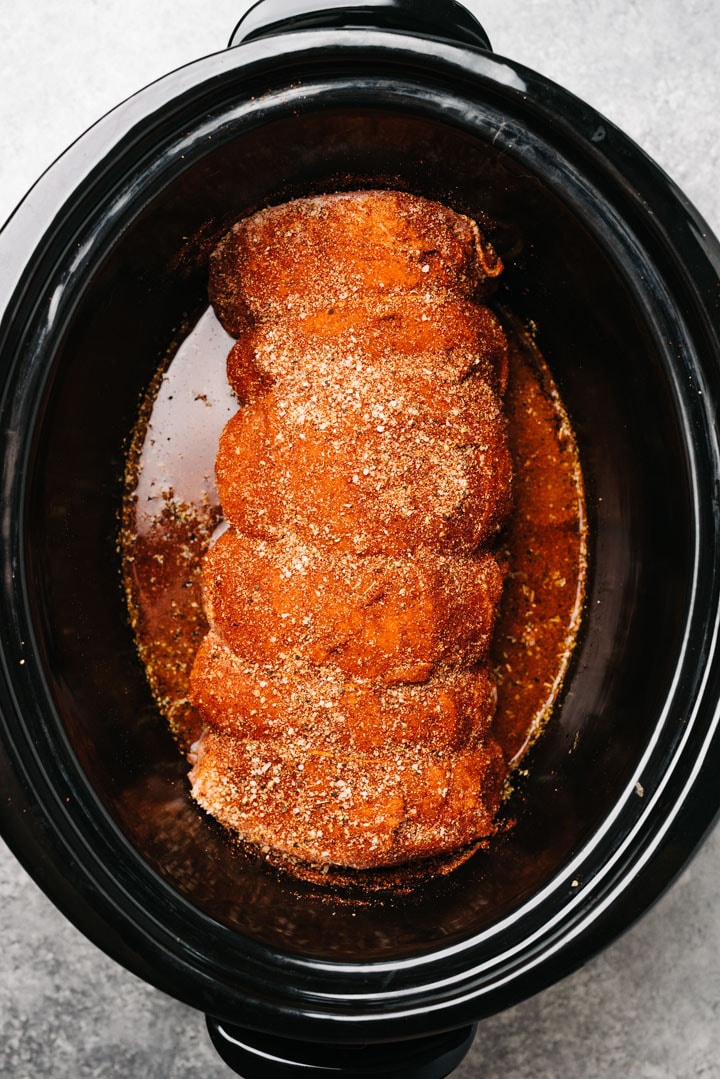 Pork shoulder rubbed with dry rub in a slow cooker.