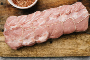 A trussed pork shoulder on a cutting board with a bowl of dry rub spice to the side.