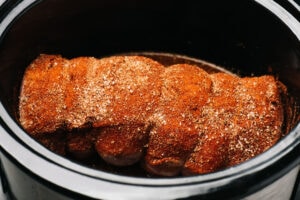 Pork shoulder rubbed with dry rub in a slow cooker.