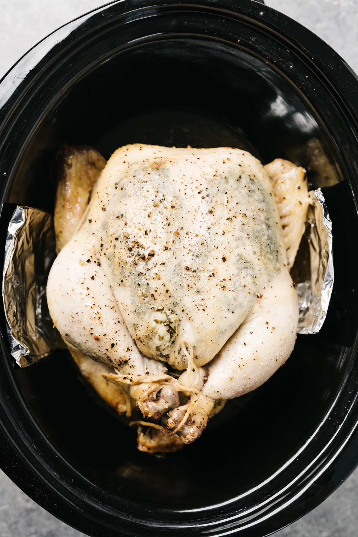 A whole chicken trussed with twine with a garlic butter rub in a slow cooker.