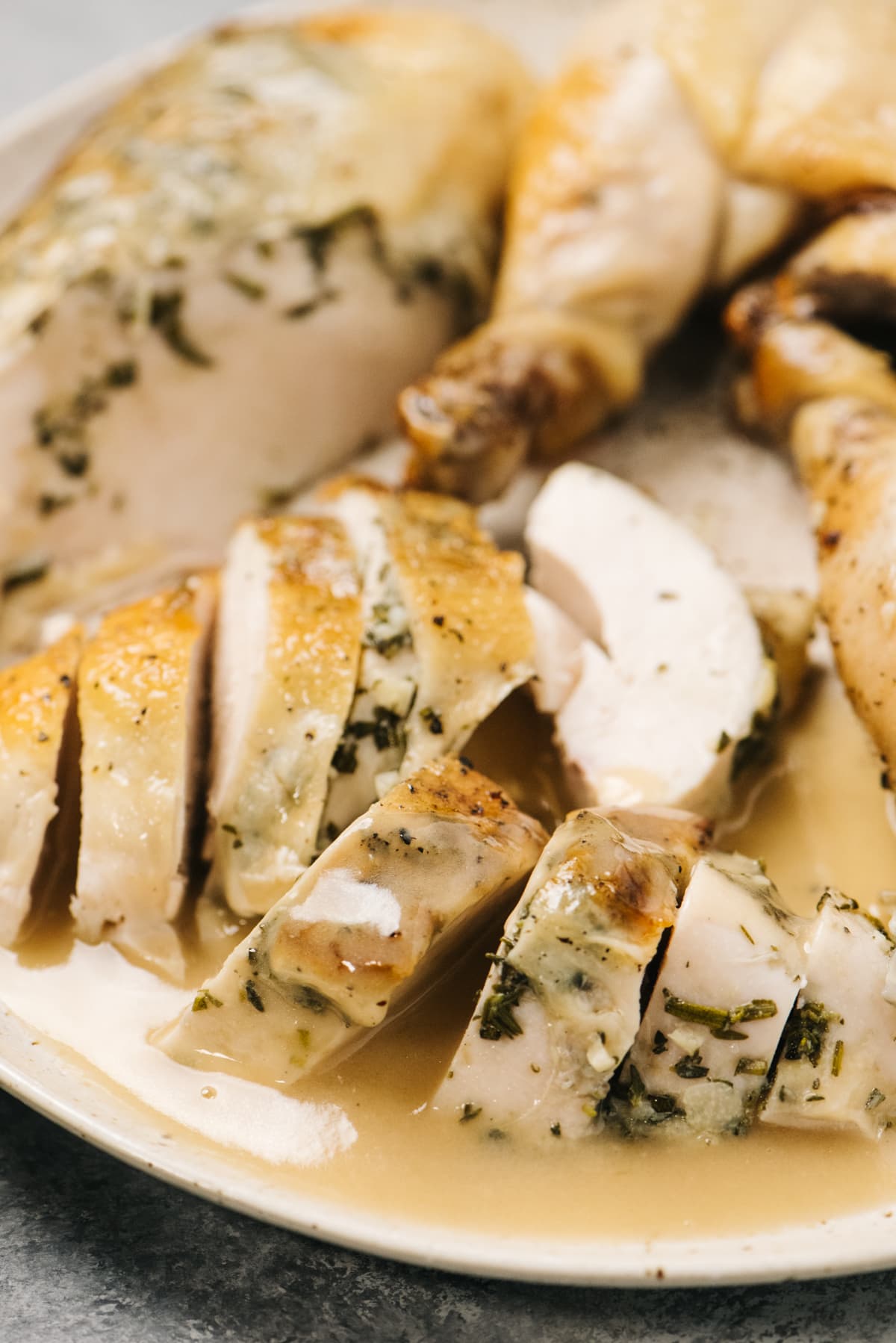Slow cooker chicken divided into slices and smothered with gravy on a tan speckled serving platter.