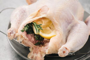 Side view, a whole chicken stuffed with lemons and fresh herbs.