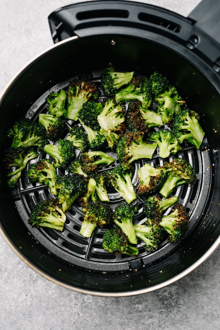 Cooked broccoli florets in single layer in the basket of an air fryer.