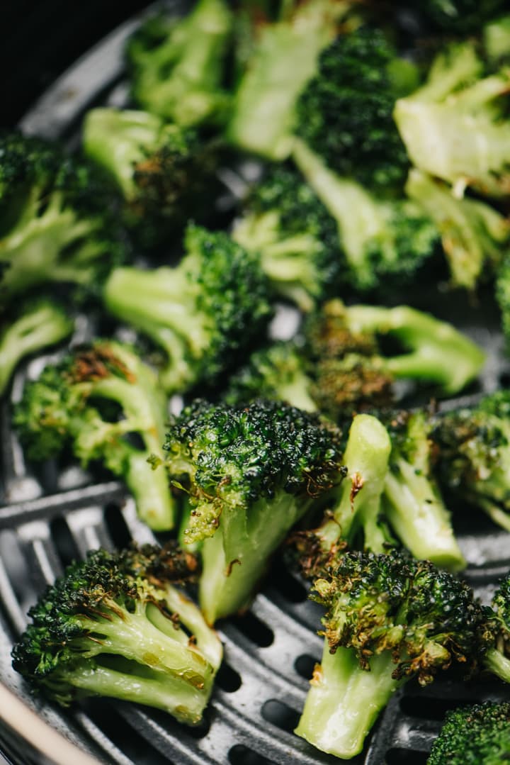 Side view, cooked broccoli florets in the basket of an air fryer.
