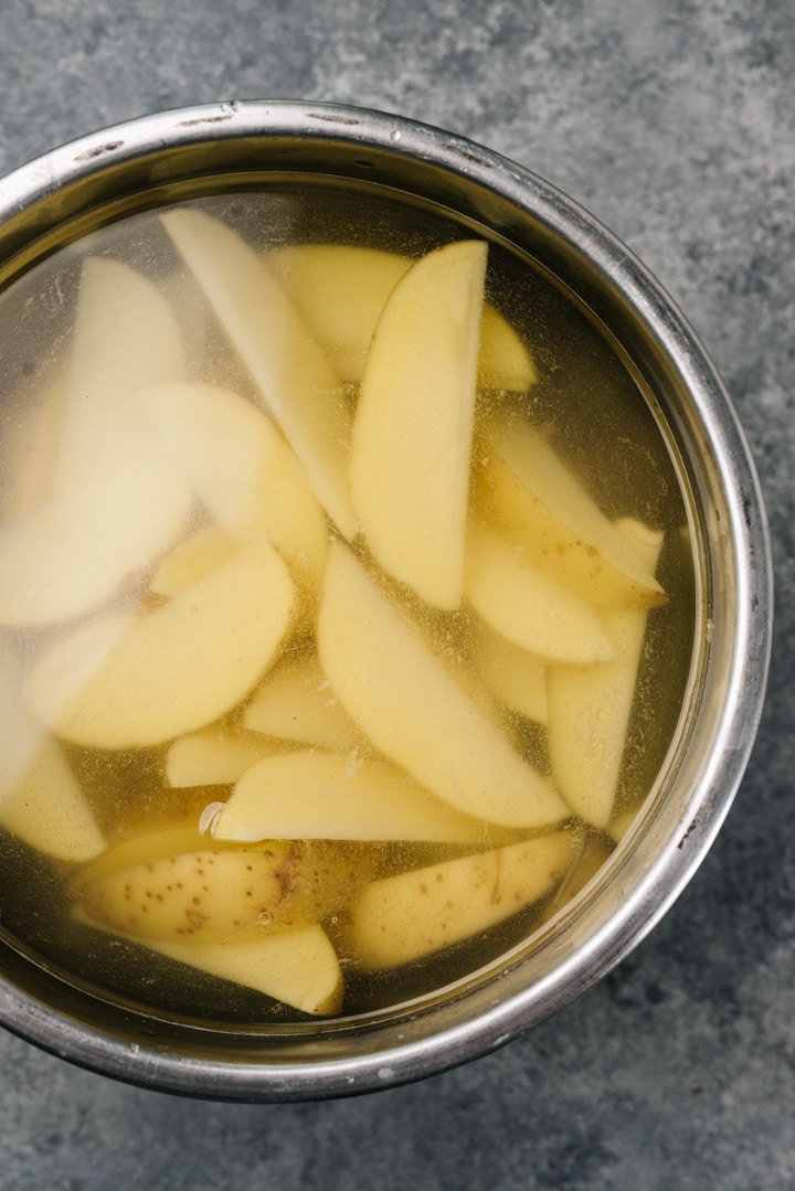 Yukon gold potato wedges soak in a bowl of cold water.