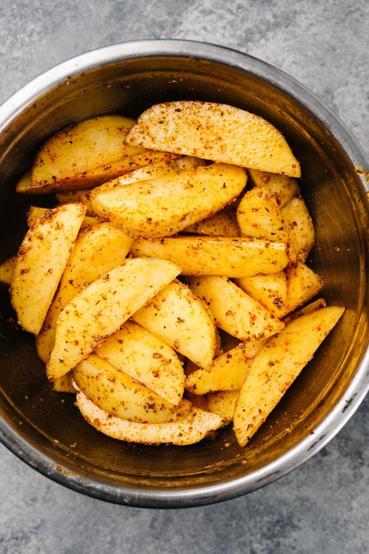 Potato wedges tossed with olive oil and seasonings in a large mixing bowl.
