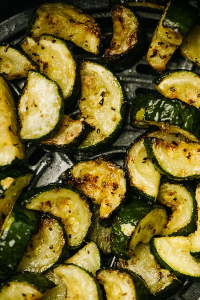 From overhead, a detail of sautéed zucchini in the basket of an air fryer.