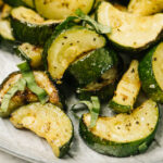 Side view, air fryer zucchini on a grey plate garnished with fresh basil.