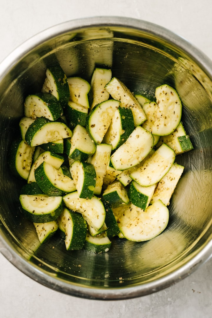 Chopped zucchini in a mixing bowl tossed with olive oil, italian seasoning, and garlic.