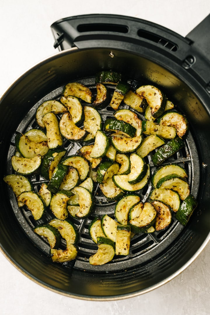 Sautéed zucchini in the basket of an air fryer.