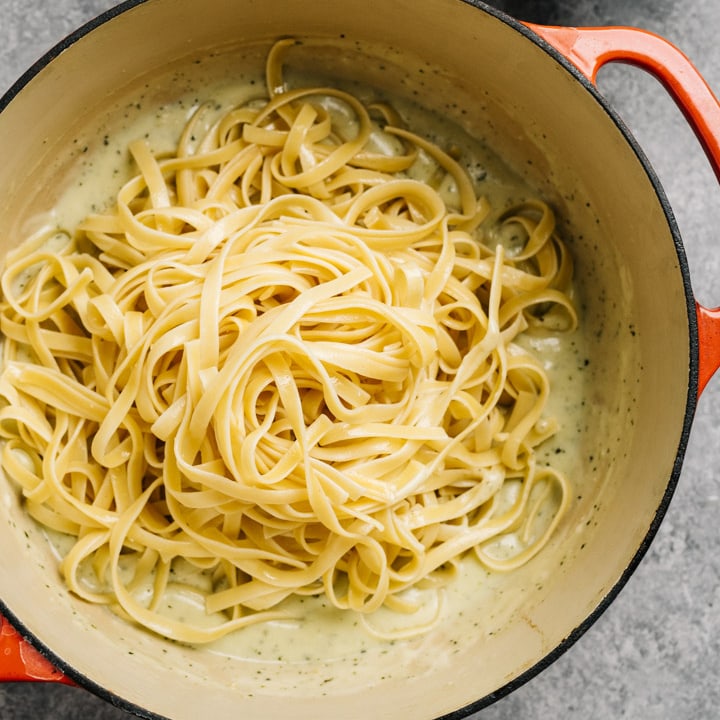 Cooked fettuccine noodles added to creamy pesto sauce in a dutch oven.