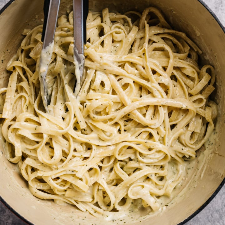 Fettuccine noodles tossed with creamy pesto sauce in a dutch oven.