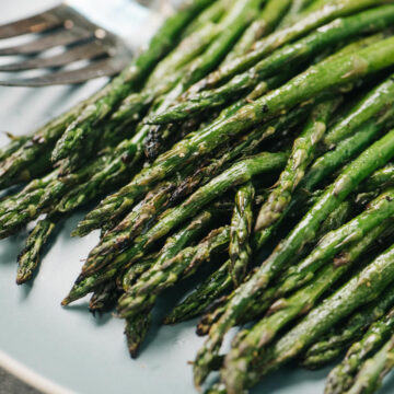Side view, grilled asparagus on a blue plate with a serving fork in the background.