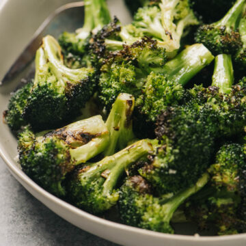 Side view, grilled broccoli florets in a tan serving bowl on a concrete background.