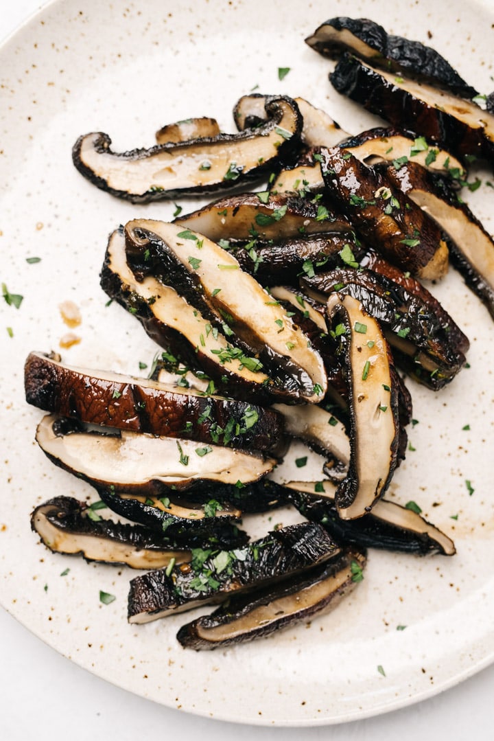 Sliced grilled portobello mushrooms on a tan speckled plate, garnished with fresh herbs.