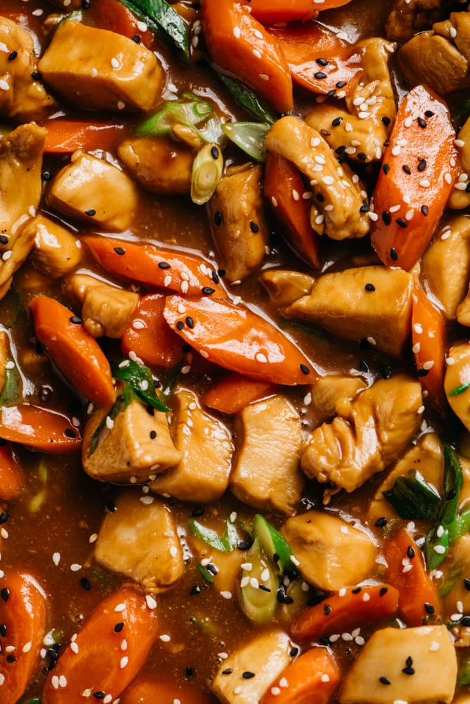 A close up detail image of honey garlic chicken with carrots, green onions, and sesame seeds.
