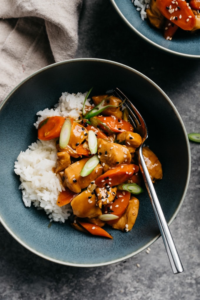 Honey garlic chicken stir fry in a blue bowl served over white rice with silver fork on a cement background.