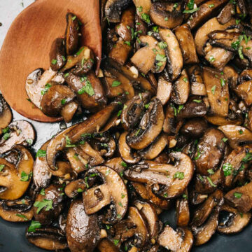 Sautéed mushrooms in a skillet with a wood serving spoon, garnished with chopped fresh herbs.