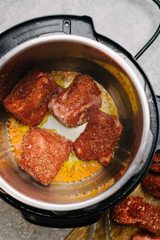 Three-inch chunks of boneless pork butt coated in dry rub being seared in a an Instant Pot.