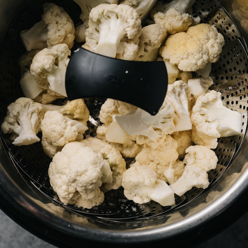 Cauliflower florets in a steamer basket in the inner pot of an Instant Pot.
