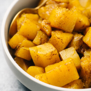 Diced and steamed instant pot butternut squash in a tan serving bowl, seasoned with spices, with a gold serving spoon.