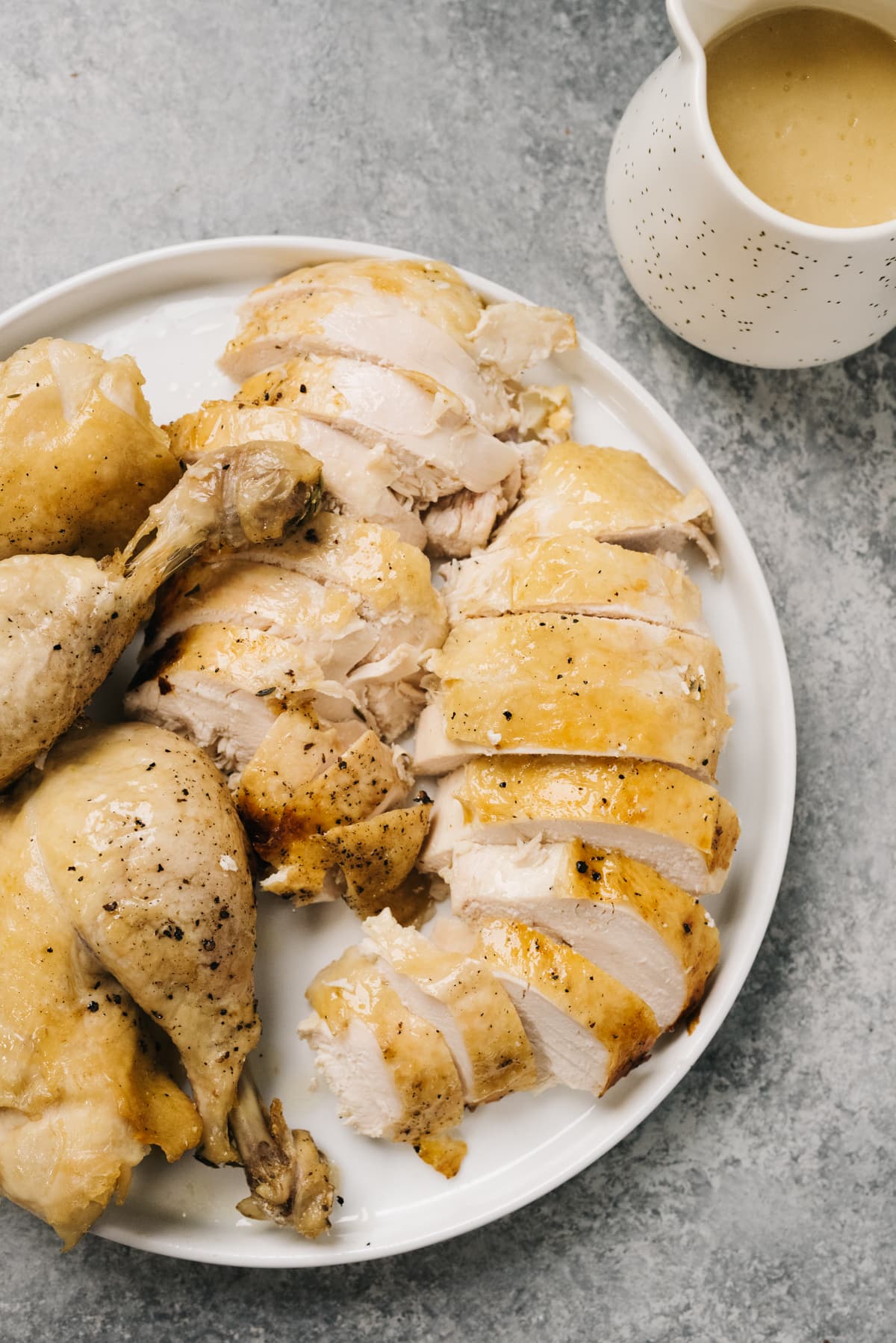 A whole chicken cooked in an instant pot carved on a white platter with a small pitcher of gravy on the side.