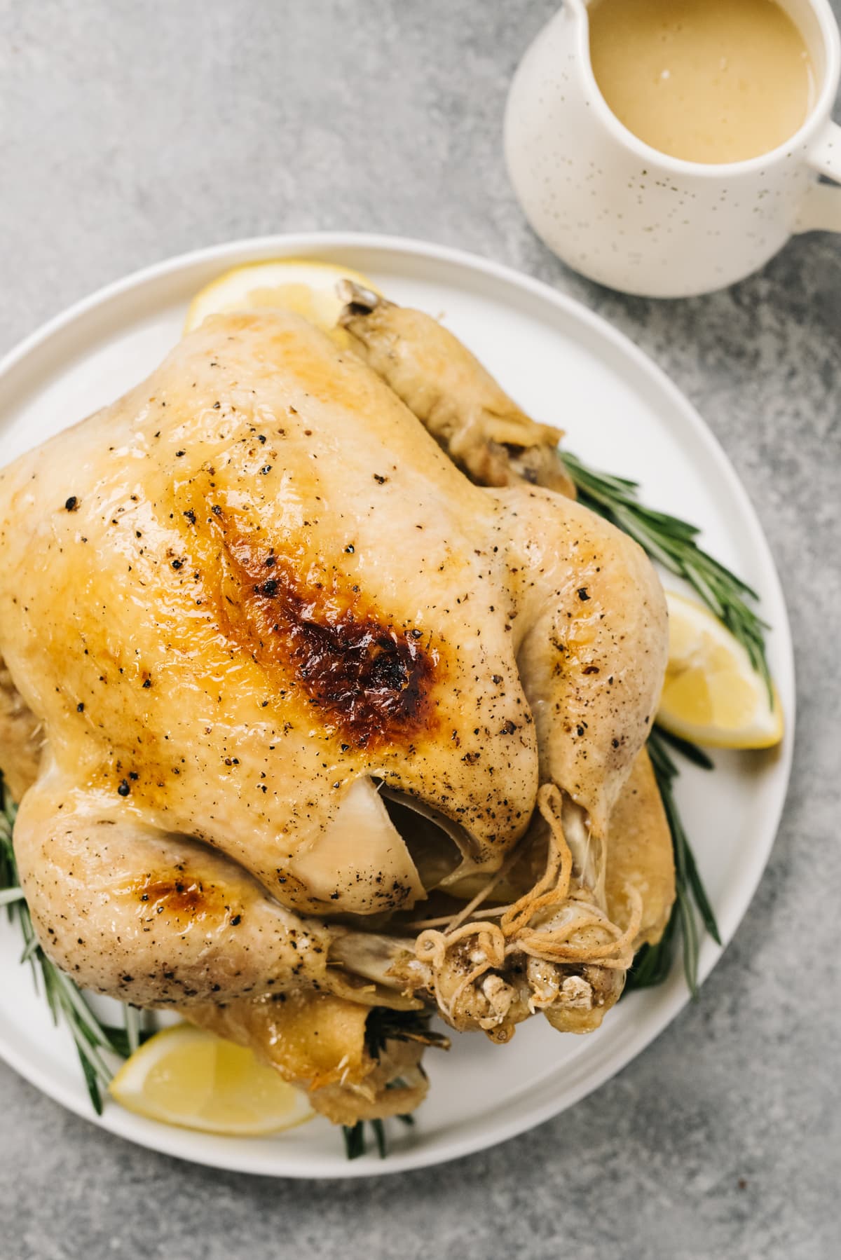 A whole chicken cooked in the instant pot on a white platter with a small pitcher of gravy on the side.