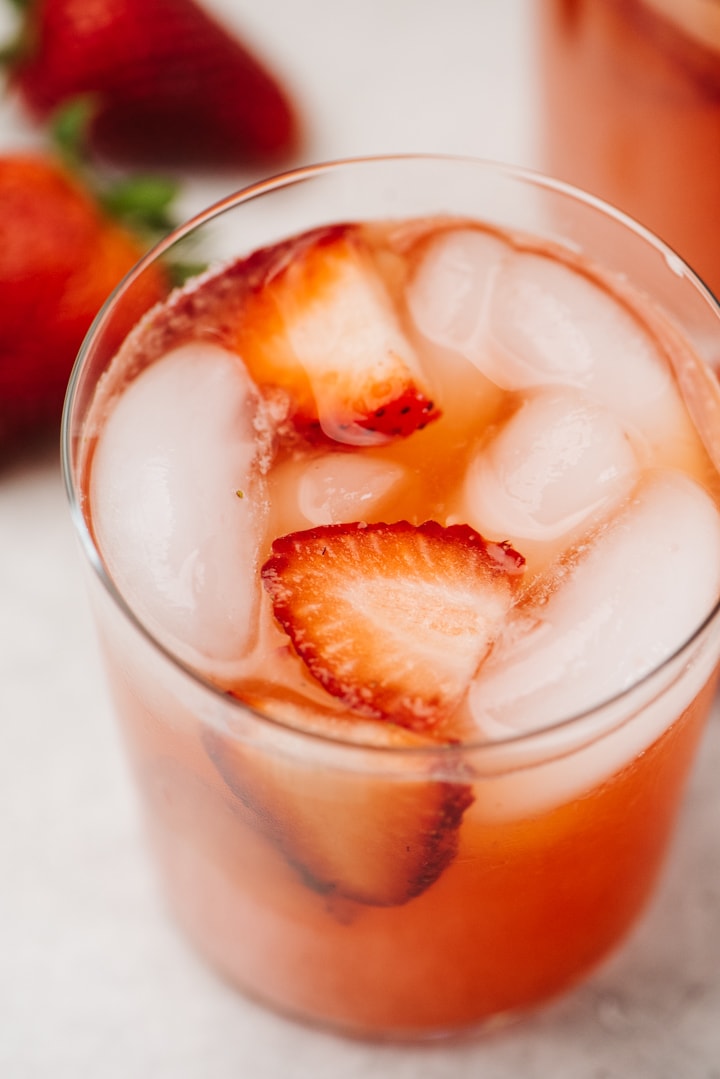 Two glasses of fresh strawberry lemonade on a concrete background with whole strawberries in the background.